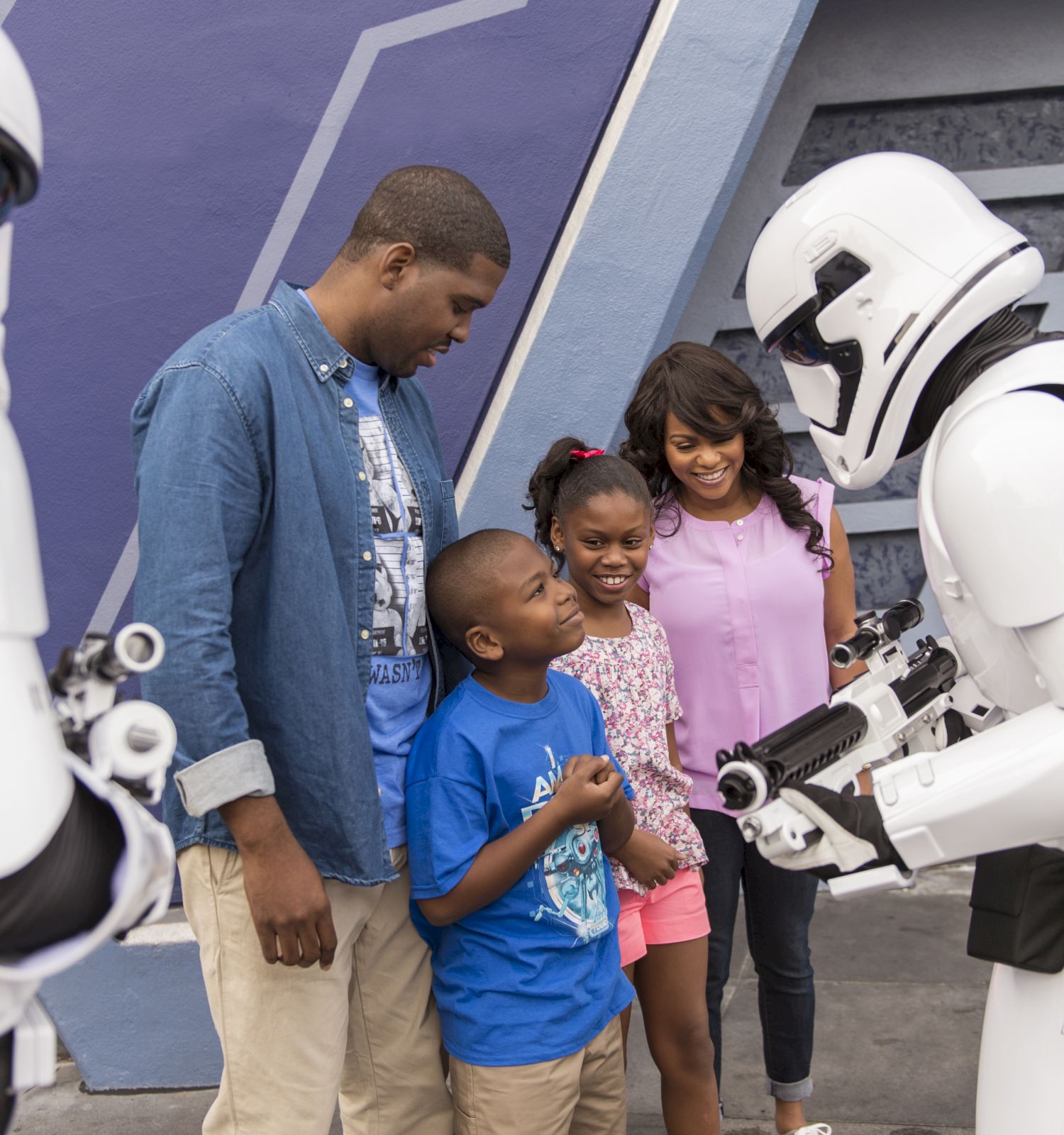 A family interacts with two people dressed as stormtroopers from Star Wars, smiling brightly in an amusement park setting.