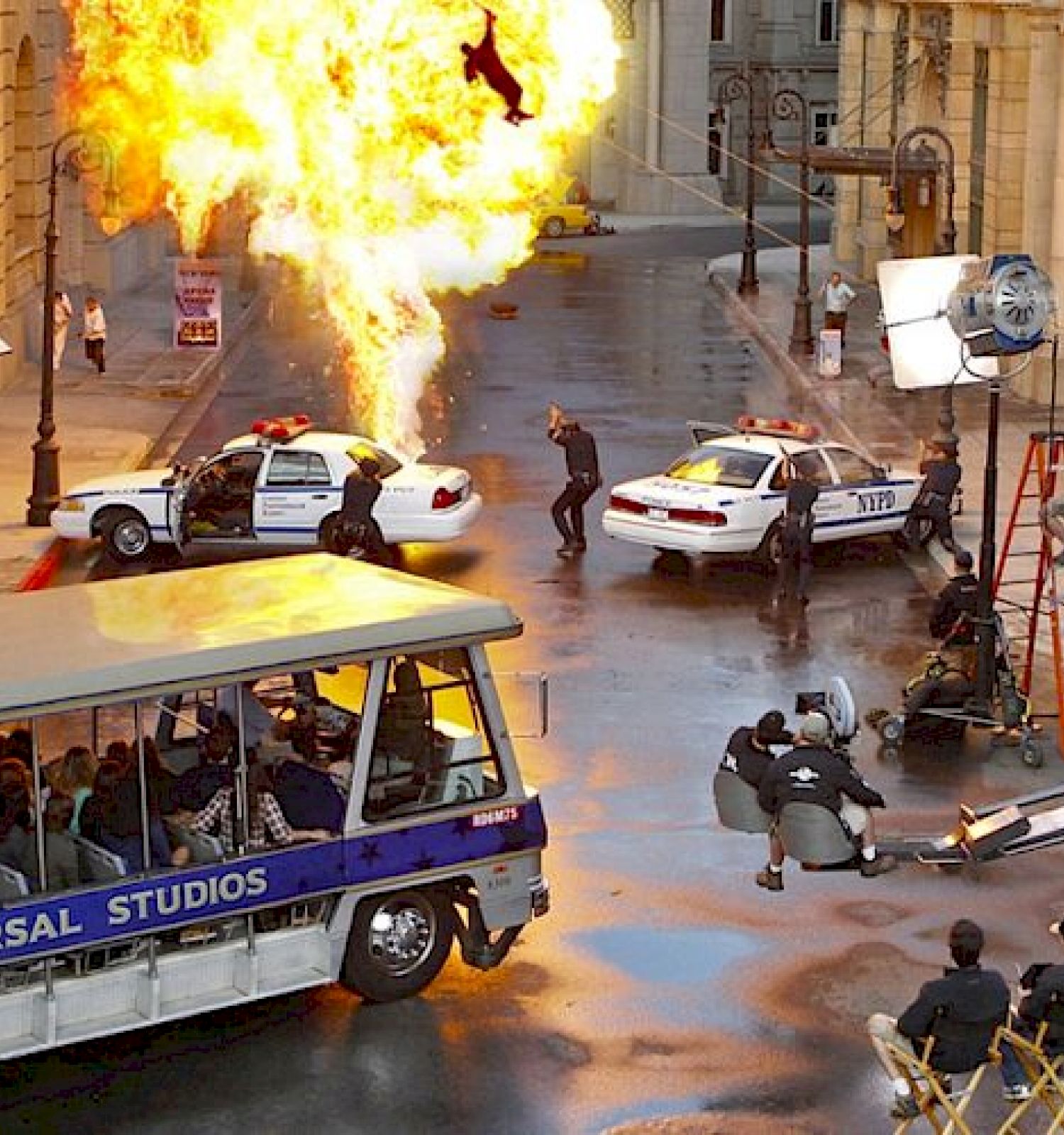A film set featuring an explosion, police cars, and crew members filming a scene; a bus marked “Universal Studios” with onlookers is visible.
