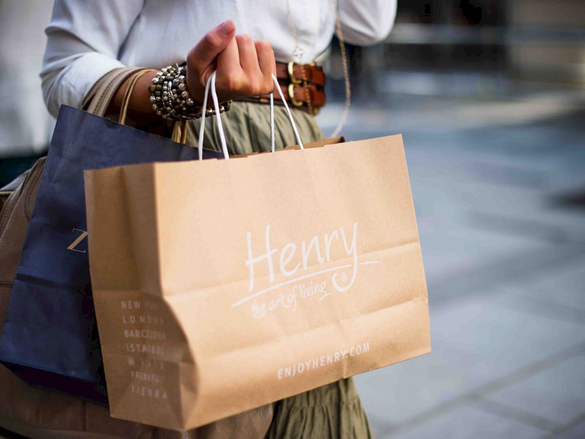 A person holding shopping bags, one of which is brown and labeled 