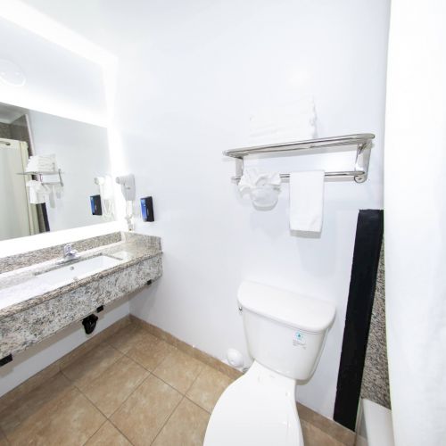A clean, modern bathroom with a toilet, a granite countertop with a sink, a large mirror, and a towel rack above the toilet, ending the sentence.
