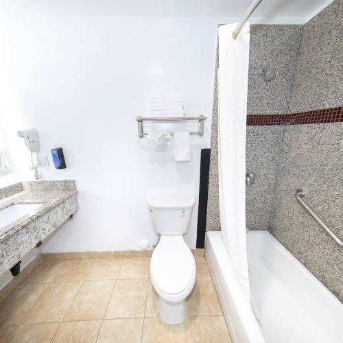 This image shows a clean modern bathroom with a sink, mirror, toilet, and bathtub with a shower curtain, featuring granite and tile finishes.
