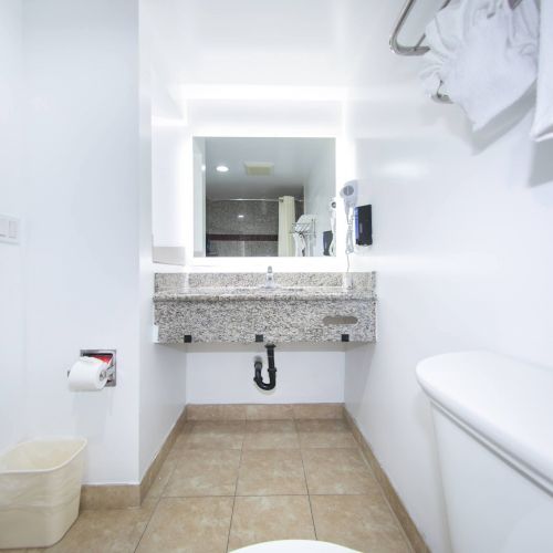 A clean, modern bathroom with a toilet, a wall-mounted sink, a mirror, towels, a trash can, and a toilet paper holder on the wall ends the sentence.