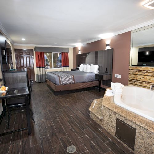 This image shows a spacious hotel room with a bed, sofa, desk, TV, and a large bathtub. The decor is modern and inviting.