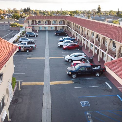 This image shows a motel with a parking lot in the center, surrounded by two rows of rooms with red-tiled roofs.