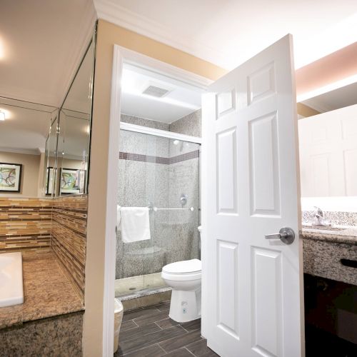 The image shows a modern bathroom with a tub, a glass-enclosed shower, a toilet, and a vanity with a mirror and granite countertop.