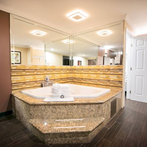 A luxurious bathroom with a large jacuzzi tub, surrounded by mirrors and tile work, towels placed on the tub, and elegant lighting fixtures.