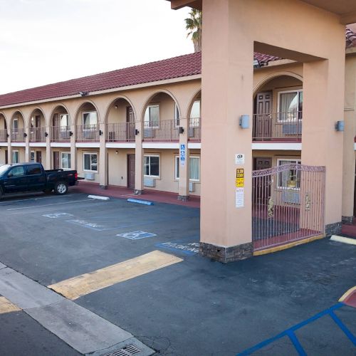 This image shows an exterior view of a two-story motel with arched balconies, parked cars, and various parking spaces including a handicapped spot.