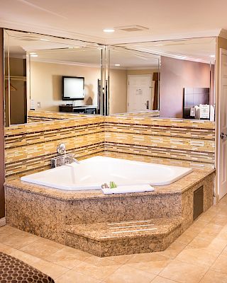 This image shows a luxurious bathroom with a large corner bathtub, surrounded by mirrors and decorated with mosaic tiles, in a spacious setting.